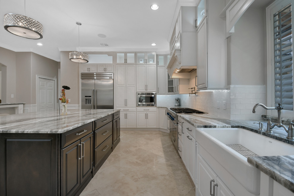 Eat-in kitchen - large traditional l-shaped porcelain tile and beige floor eat-in kitchen idea in Orlando with an undermount sink, raised-panel cabinets, white cabinets, marble countertops, white backsplash, subway tile backsplash, stainless steel appliances and an island