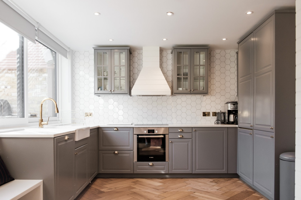 Medium sized traditional u-shaped kitchen/diner in London with a belfast sink, shaker cabinets, grey cabinets, marble worktops, white splashback, ceramic splashback, stainless steel appliances, dark hardwood flooring, no island, brown floors and white worktops.