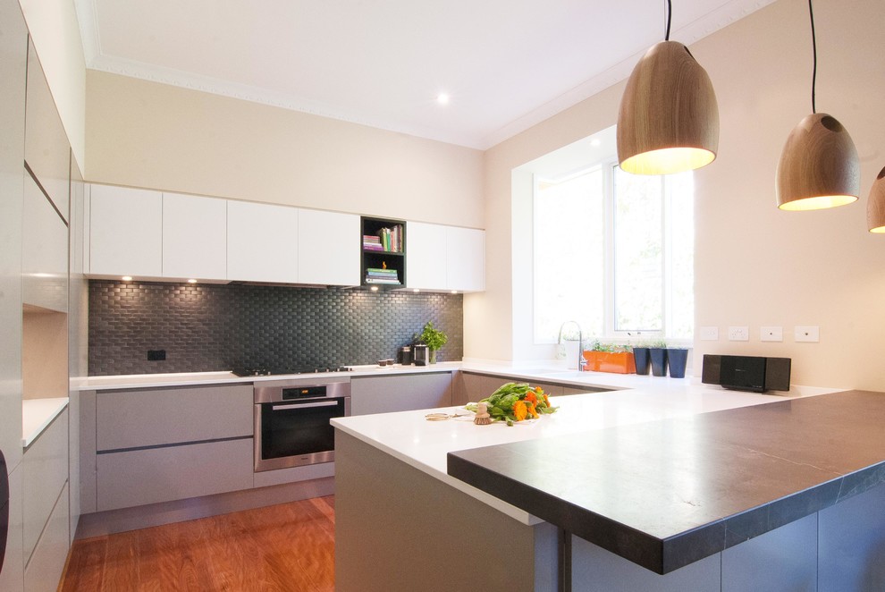 Medium sized contemporary u-shaped open plan kitchen in Melbourne with an integrated sink, grey cabinets, marble worktops, black splashback, mosaic tiled splashback, stainless steel appliances, light hardwood flooring and a breakfast bar.