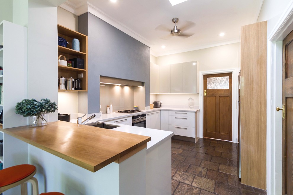 Photo of a medium sized retro u-shaped kitchen pantry in Melbourne with flat-panel cabinets, white cabinets, engineered stone countertops, grey splashback, glass sheet splashback, stainless steel appliances, slate flooring, brown floors and a submerged sink.