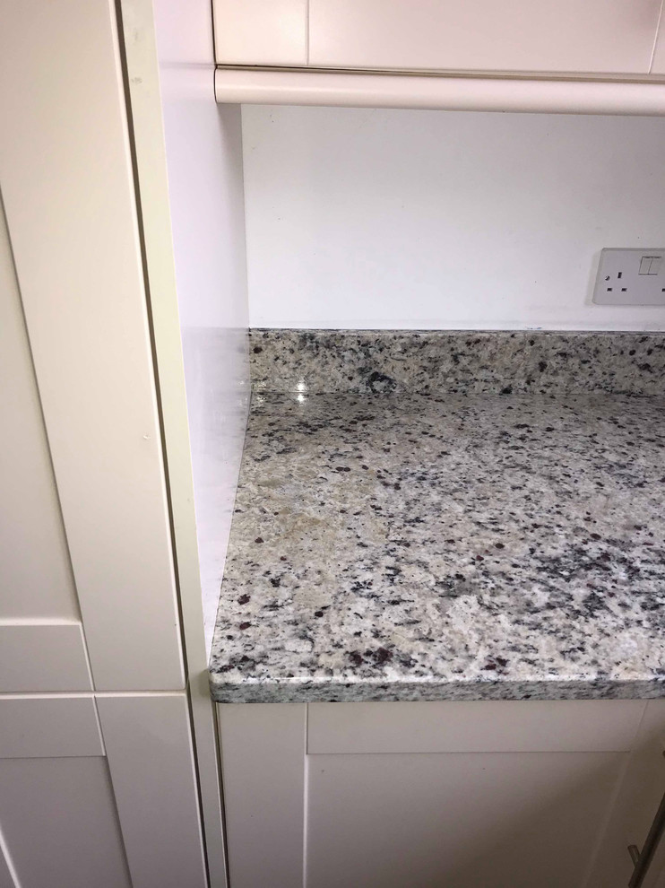 Modern inredning av ett mellanstort vit vitt kök, med en dubbel diskho, släta luckor, vita skåp, granitbänkskiva, stänkskydd med metallisk yta, stänkskydd i metallkakel, rostfria vitvaror, klinkergolv i porslin, en köksö och grått golv