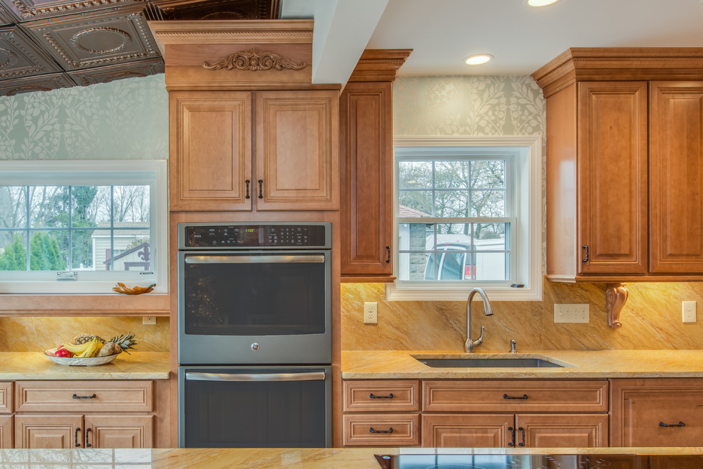 Large elegant l-shaped light wood floor and brown floor enclosed kitchen photo in Boston with an undermount sink, raised-panel cabinets, medium tone wood cabinets, granite countertops, yellow backsplash, stone slab backsplash, stainless steel appliances and an island