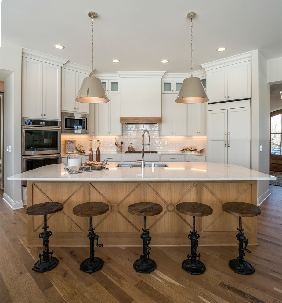 Design ideas for a traditional kitchen in Minneapolis with a submerged sink, shaker cabinets, white cabinets, white splashback, metro tiled splashback, integrated appliances, light hardwood flooring, an island and white worktops.