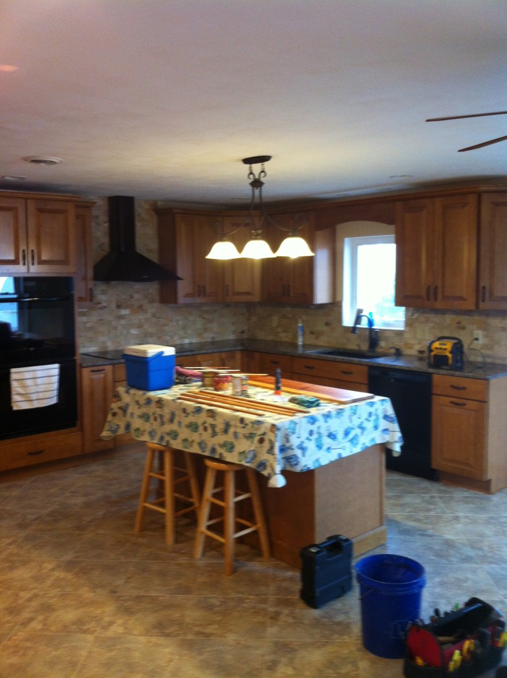 Inredning av ett modernt mellanstort kök, med en undermonterad diskho, luckor med upphöjd panel, skåp i mellenmörkt trä, granitbänkskiva, beige stänkskydd, stänkskydd i stenkakel, svarta vitvaror, vinylgolv och en köksö