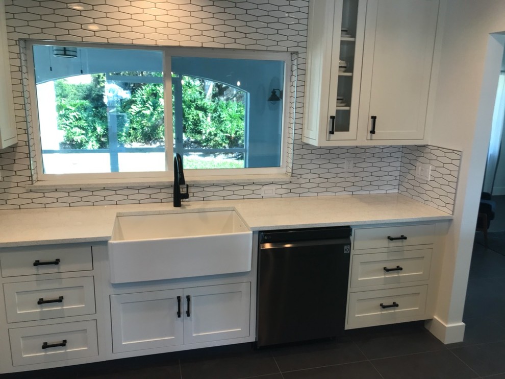 Photo of a medium sized midcentury l-shaped kitchen in Tampa with a belfast sink, shaker cabinets, white cabinets, engineered stone countertops, white splashback, porcelain splashback, stainless steel appliances, porcelain flooring, an island, grey floors and white worktops.