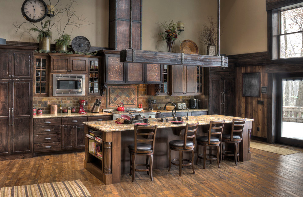 Inspiration for a rustic galley medium tone wood floor open concept kitchen remodel in Minneapolis with a farmhouse sink, raised-panel cabinets, medium tone wood cabinets, granite countertops, brown backsplash, stone tile backsplash, paneled appliances and an island