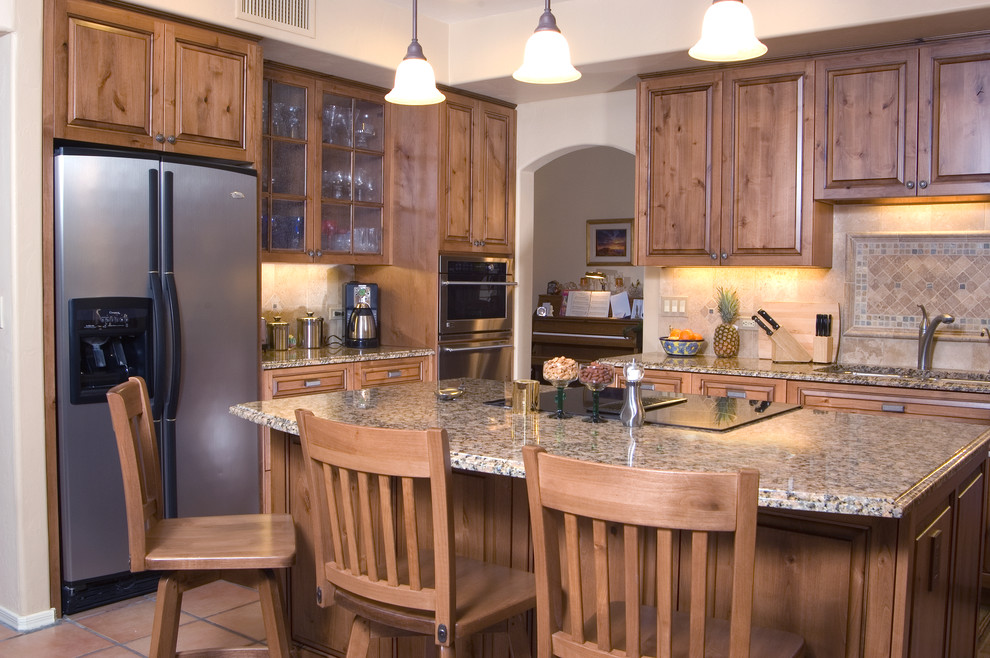 Kitchen pantry - large traditional l-shaped terra-cotta tile kitchen pantry idea in Phoenix with a double-bowl sink, raised-panel cabinets, medium tone wood cabinets, granite countertops, beige backsplash, stone slab backsplash, stainless steel appliances and an island