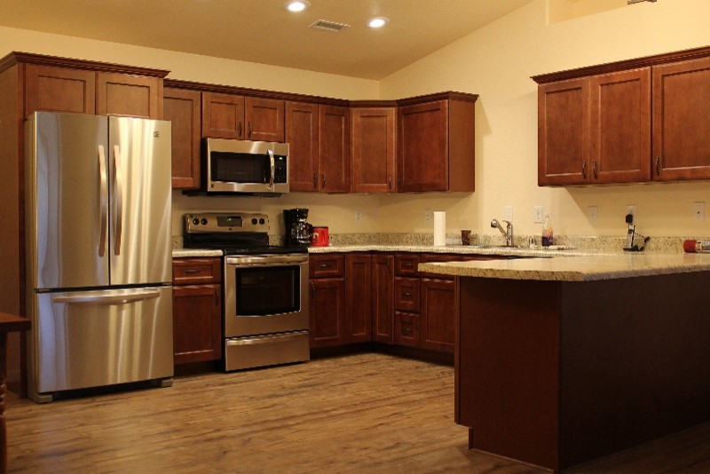 Exempel på ett mellanstort modernt kök, med en undermonterad diskho, skåp i shakerstil, skåp i mellenmörkt trä, granitbänkskiva, svart stänkskydd, stänkskydd i keramik, rostfria vitvaror, ljust trägolv och en köksö