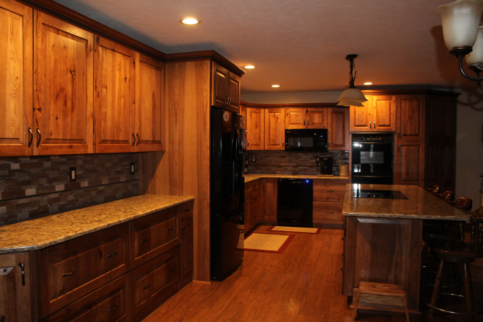 Idéer för stora rustika brunt kök, med en undermonterad diskho, luckor med upphöjd panel, bruna skåp, bänkskiva i kvartsit, stänkskydd med metallisk yta, svarta vitvaror, mellanmörkt trägolv, en köksö och brunt golv