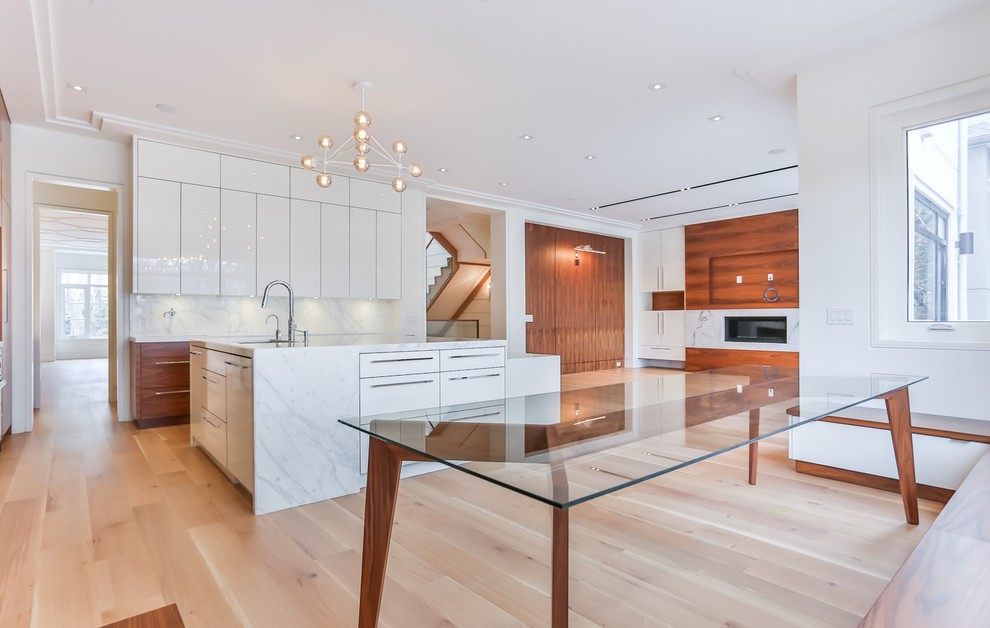 Large trendy galley light wood floor kitchen photo in Toronto with an undermount sink, flat-panel cabinets, marble countertops, white backsplash, marble backsplash, white appliances, an island and white countertops