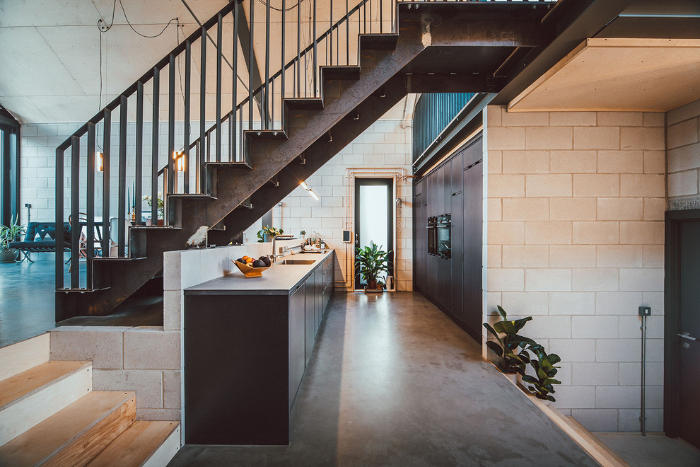 Foto på ett mellanstort industriellt grå kök, med en nedsänkt diskho, släta luckor, grå skåp, bänkskiva i rostfritt stål, integrerade vitvaror, betonggolv och grått golv
