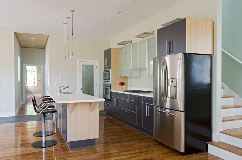 Immagine di una cucina design di medie dimensioni con lavello da incasso, ante lisce, ante nere, top in superficie solida, paraspruzzi bianco, elettrodomestici in acciaio inossidabile e pavimento in legno massello medio