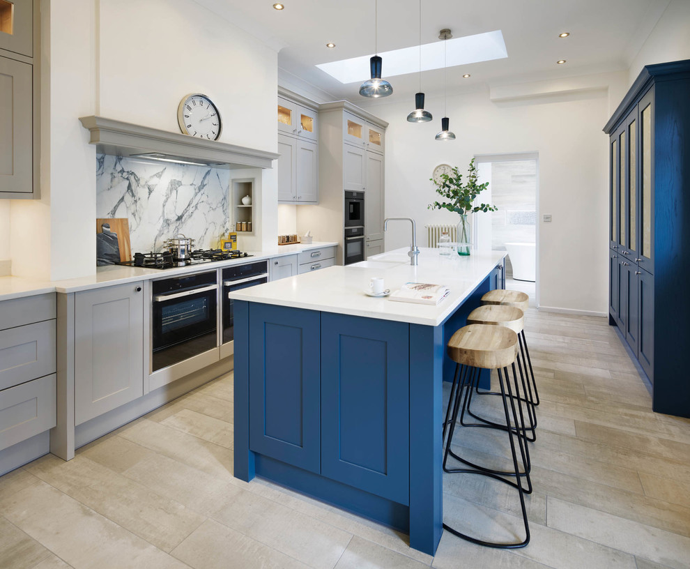 This is an example of a rural single-wall kitchen in Other with a belfast sink, shaker cabinets, grey cabinets, grey splashback, stone slab splashback, black appliances, an island, beige floors and white worktops.