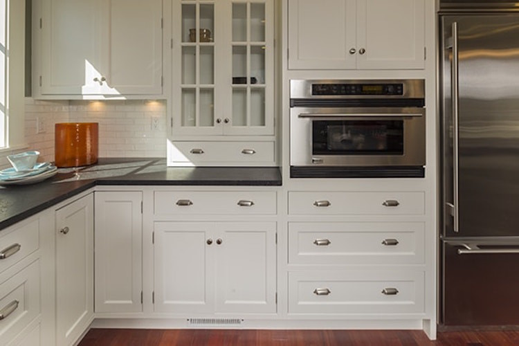 Inspiration for a medium sized traditional u-shaped kitchen/diner in San Francisco with a belfast sink, recessed-panel cabinets, white cabinets, composite countertops, white splashback, metro tiled splashback, stainless steel appliances, dark hardwood flooring, an island and brown floors.