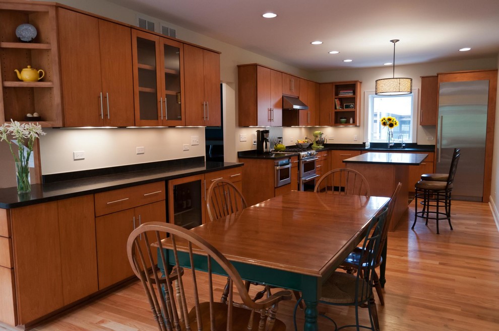 Cette image montre une cuisine américaine en L et bois brun avec un évier encastré, un placard à porte plane, un plan de travail en surface solide, une crédence blanche, un électroménager en acier inoxydable, un sol en bois brun et îlot.
