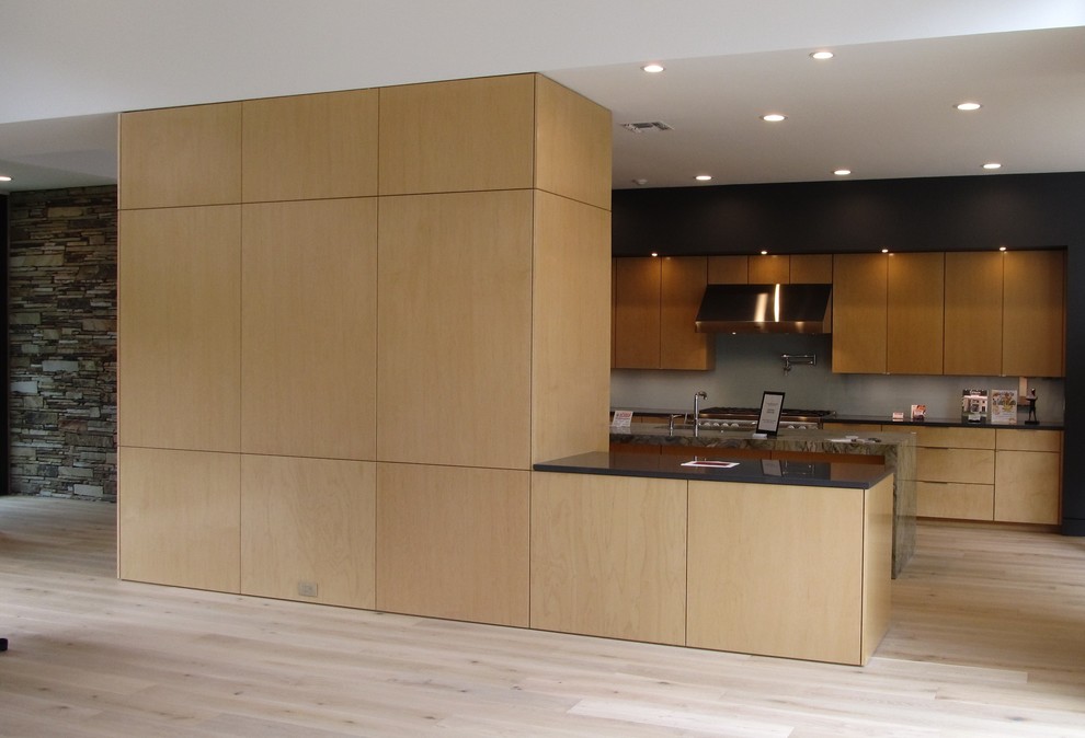 Modern inredning av ett mellanstort kök, med en undermonterad diskho, släta luckor, skåp i ljust trä, granitbänkskiva, grått stänkskydd, glaspanel som stänkskydd, rostfria vitvaror, ljust trägolv och en köksö