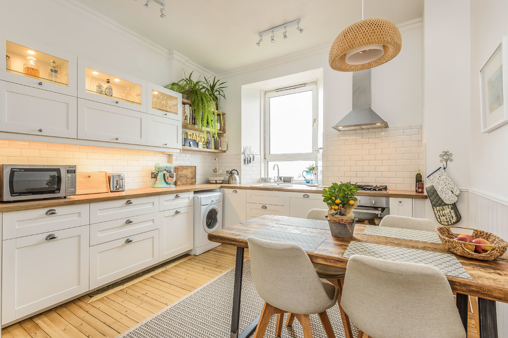 Inspiration for a mid-sized scandinavian l-shaped medium tone wood floor and brown floor eat-in kitchen remodel in Edinburgh with a drop-in sink, shaker cabinets, white cabinets, wood countertops, white backsplash, ceramic backsplash, no island, white countertops and stainless steel appliances