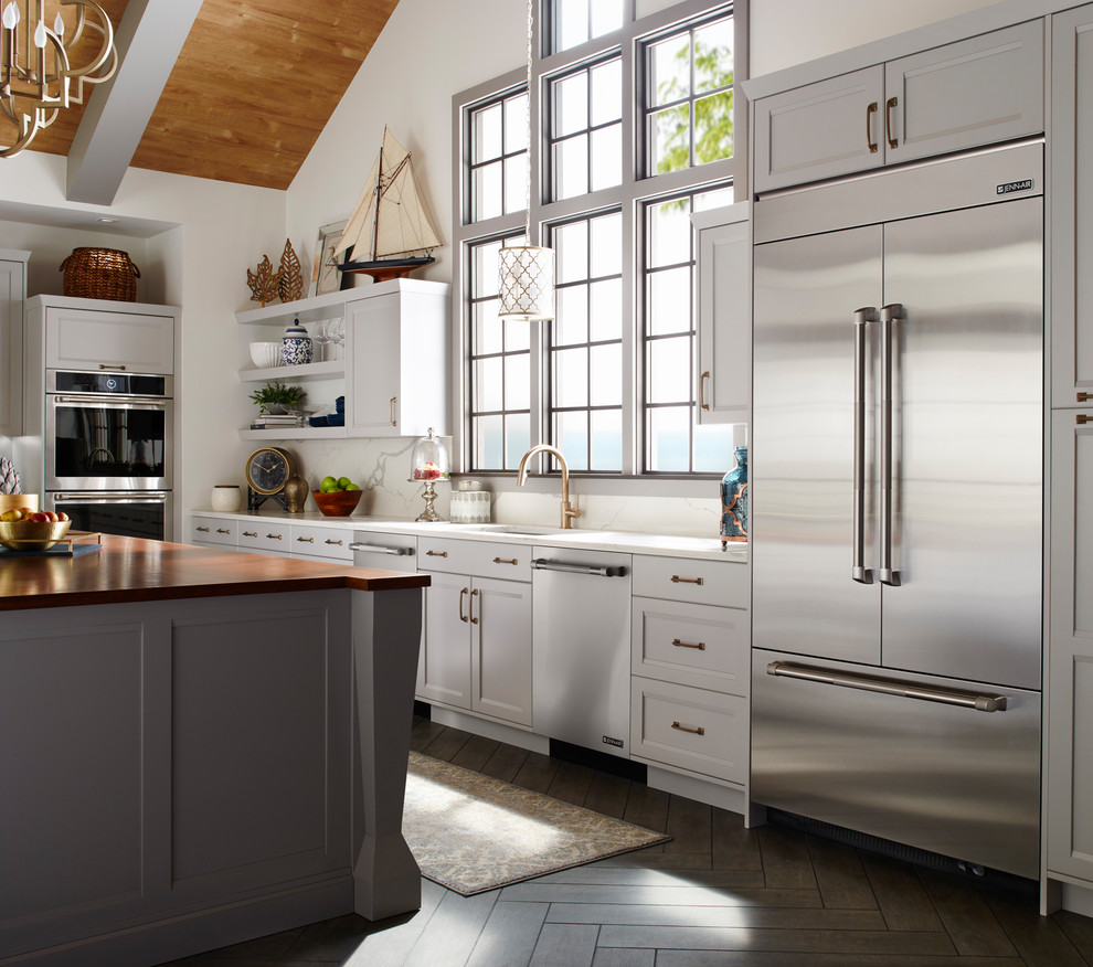 Exempel på ett klassiskt l-kök, med en undermonterad diskho, luckor med infälld panel, vita skåp, vitt stänkskydd, stänkskydd i marmor, rostfria vitvaror, mörkt trägolv, en köksö och brunt golv