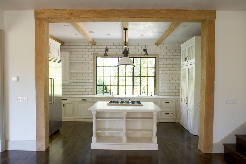 Bild på ett mellanstort vintage kök, med en undermonterad diskho, luckor med upphöjd panel, vita skåp, marmorbänkskiva, vitt stänkskydd, stänkskydd i tunnelbanekakel, rostfria vitvaror, mörkt trägolv, en köksö och brunt golv