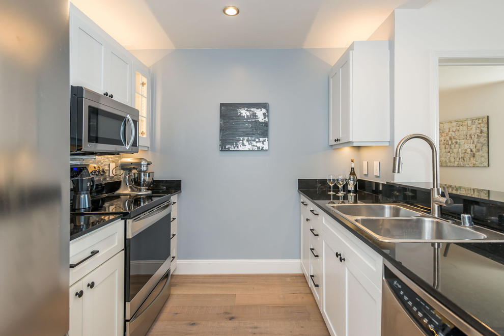 Small trendy galley light wood floor enclosed kitchen photo in San Francisco with a double-bowl sink, shaker cabinets, white cabinets, granite countertops, metallic backsplash, metal backsplash, stainless steel appliances and no island