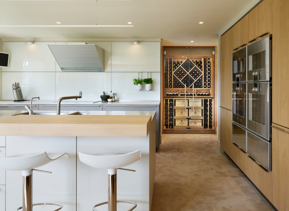 Bild på ett mellanstort funkis kök, med en dubbel diskho, släta luckor, vitt stänkskydd, rostfria vitvaror, en köksö, skåp i ljust trä och beiget golv