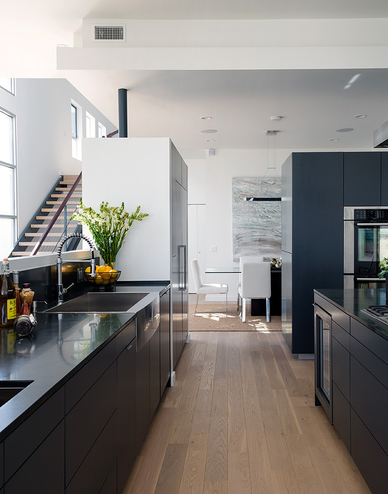 Große Moderne Wohnküche mit Landhausspüle, flächenbündigen Schrankfronten, Küchengeräten aus Edelstahl, braunem Holzboden und zwei Kücheninseln in Los Angeles