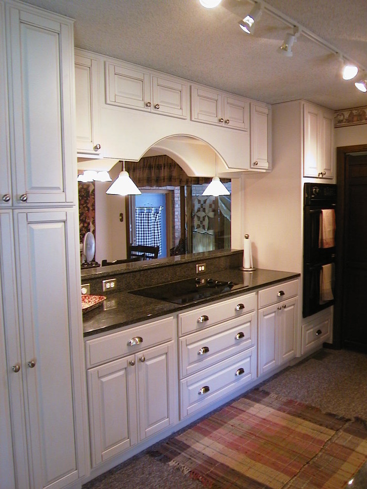 Modelo de cocina comedor tradicional de tamaño medio con armarios con paneles con relieve, puertas de armario blancas, encimera de granito y electrodomésticos negros