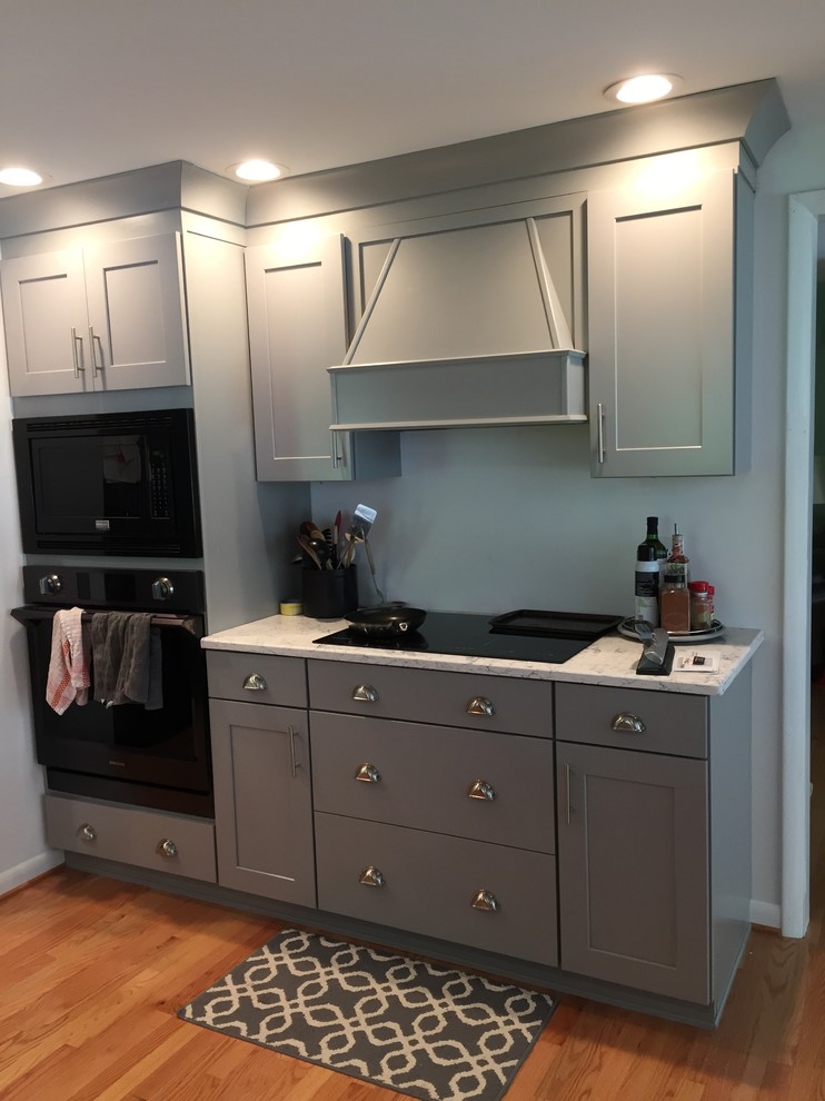 Inspiration for a medium sized traditional l-shaped open plan kitchen in DC Metro with a belfast sink, raised-panel cabinets, grey cabinets, granite worktops, black appliances, medium hardwood flooring, a breakfast bar and brown floors.