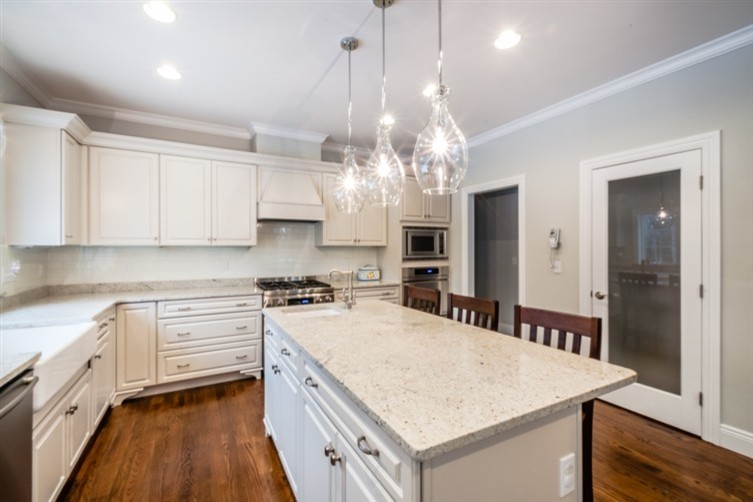 Example of a large classic l-shaped medium tone wood floor eat-in kitchen design in New York with a farmhouse sink, raised-panel cabinets, white cabinets, granite countertops, white backsplash, subway tile backsplash, stainless steel appliances and an island