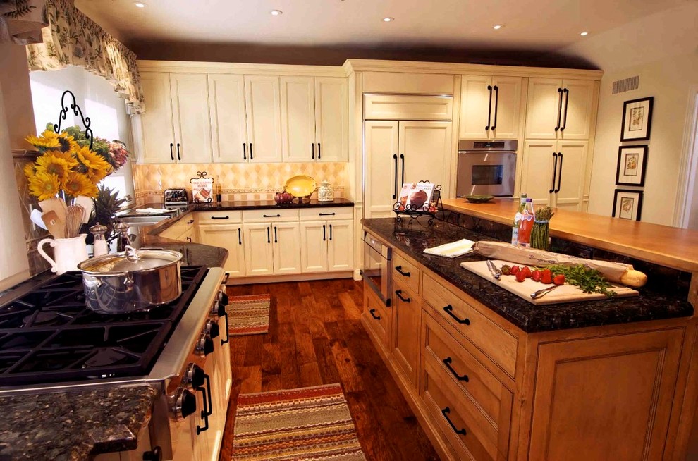 Exempel på ett avskilt, stort lantligt l-kök, med en dubbel diskho, luckor med infälld panel, vita skåp, granitbänkskiva, beige stänkskydd, stänkskydd i travertin, integrerade vitvaror, mörkt trägolv, en köksö och brunt golv
