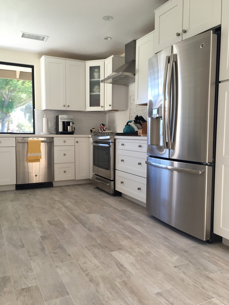 Klassische Wohnküche mit Schrankfronten mit vertiefter Füllung, weißen Schränken, Küchenrückwand in Beige, Rückwand aus Keramikfliesen, Küchengeräten aus Edelstahl und hellem Holzboden in Los Angeles