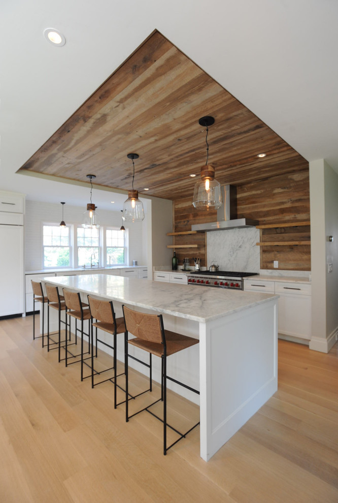Mid-sized beach style l-shaped light wood floor and beige floor open concept kitchen photo in Boston with an undermount sink, shaker cabinets, white cabinets, marble countertops, wood backsplash, stainless steel appliances and an island