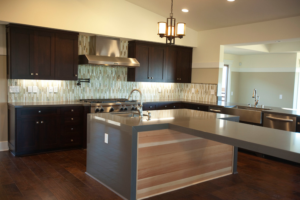 Example of a large transitional l-shaped dark wood floor eat-in kitchen design in Los Angeles with a farmhouse sink, shaker cabinets, dark wood cabinets, solid surface countertops, multicolored backsplash, matchstick tile backsplash, stainless steel appliances and an island
