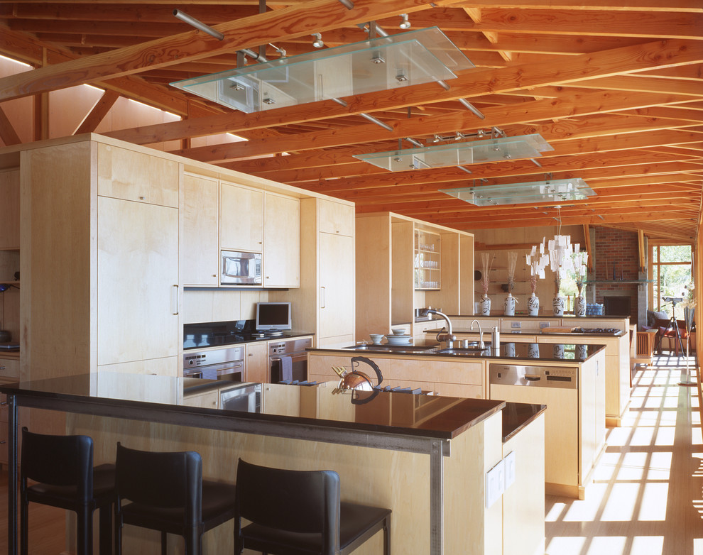 Immagine di una cucina industriale con lavello sottopiano, ante lisce, ante in legno chiaro e elettrodomestici in acciaio inossidabile