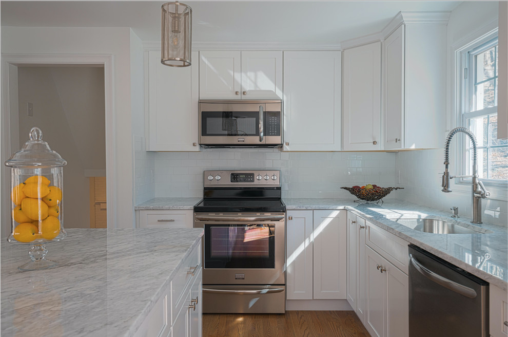 Klassisk inredning av ett mellanstort kök, med en undermonterad diskho, skåp i shakerstil, vita skåp, marmorbänkskiva, vitt stänkskydd, stänkskydd i tunnelbanekakel, rostfria vitvaror, mellanmörkt trägolv, en köksö och brunt golv