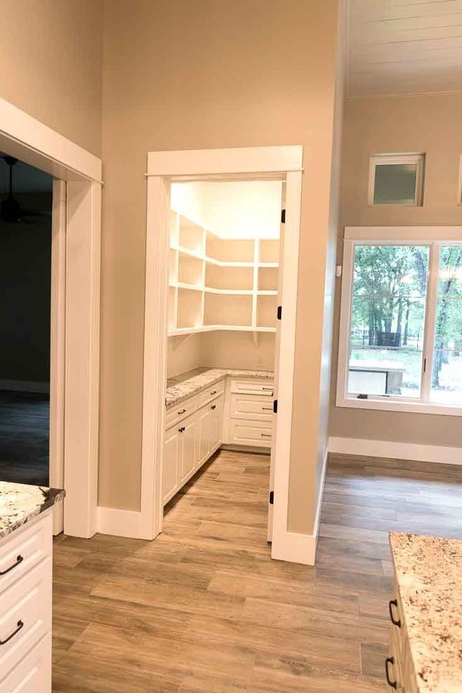 Mittelgroße Landhausstil Küche in U-Form mit Vorratsschrank, profilierten Schrankfronten, weißen Schränken, Granit-Arbeitsplatte, braunem Holzboden, Kücheninsel und beigem Boden in Austin