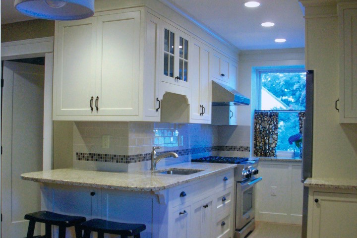 This is an example of a small traditional galley enclosed kitchen in Boston with a submerged sink, shaker cabinets, white cabinets, granite worktops, beige splashback, metro tiled splashback, stainless steel appliances, light hardwood flooring, a breakfast bar, beige floors and white worktops.