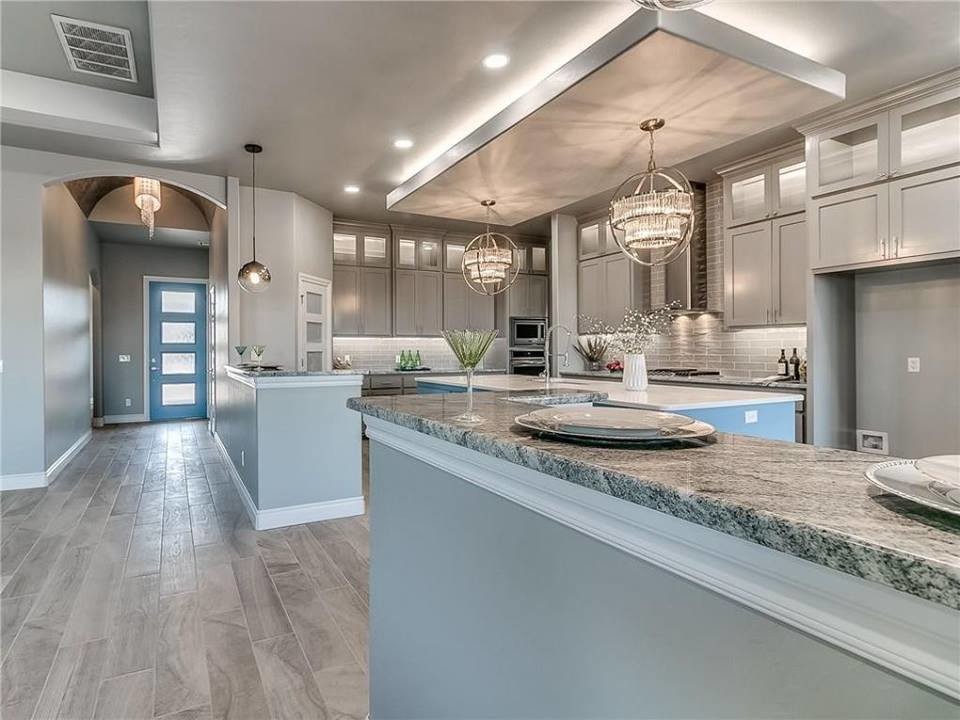 Large transitional l-shaped medium tone wood floor and gray floor open concept kitchen photo in Oklahoma City with an undermount sink, shaker cabinets, gray cabinets, granite countertops, gray backsplash, subway tile backsplash, stainless steel appliances, an island and multicolored countertops