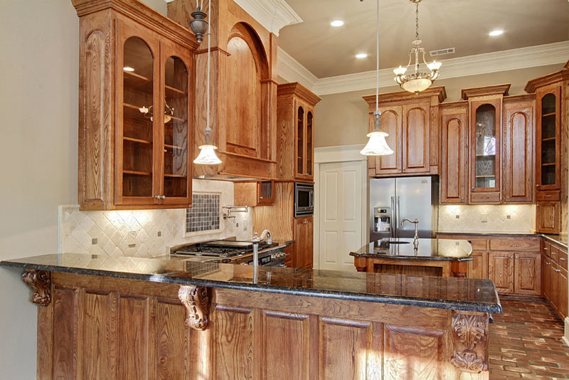 Immagine di una cucina classica di medie dimensioni con ante di vetro, ante in legno scuro, top in granito, paraspruzzi bianco, elettrodomestici in acciaio inossidabile, pavimento in mattoni e lavello a doppia vasca