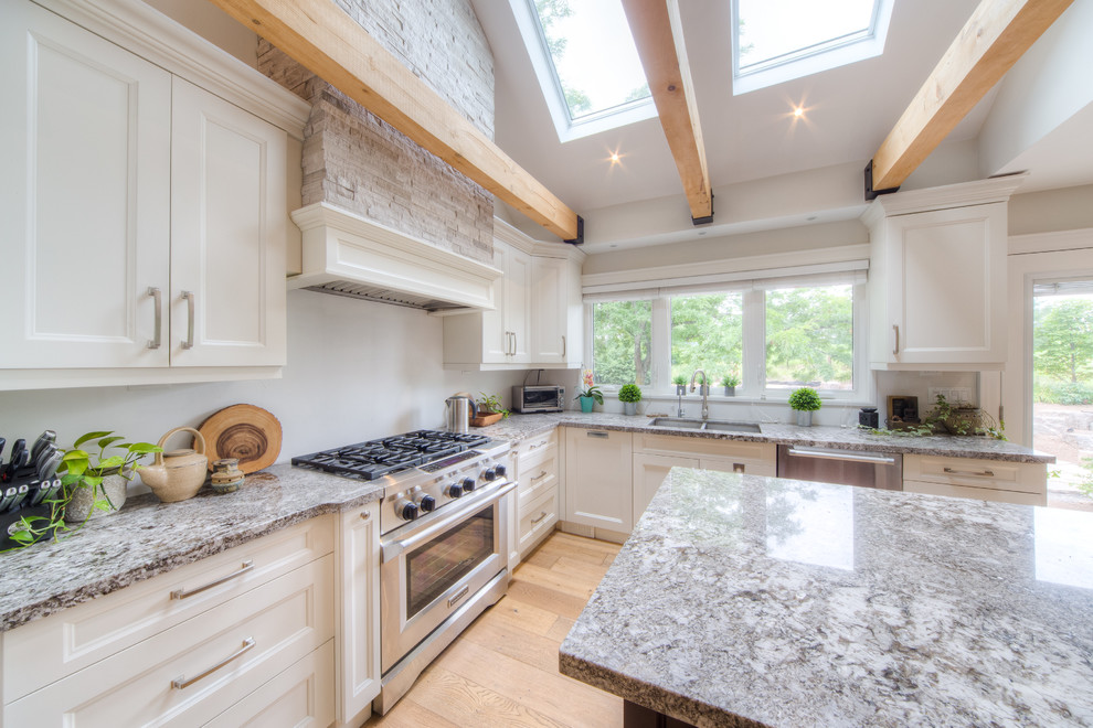 Bild på ett avskilt, stort vintage grå grått l-kök, med en dubbel diskho, luckor med infälld panel, vita skåp, granitbänkskiva, rostfria vitvaror, ljust trägolv, en köksö och beiget golv