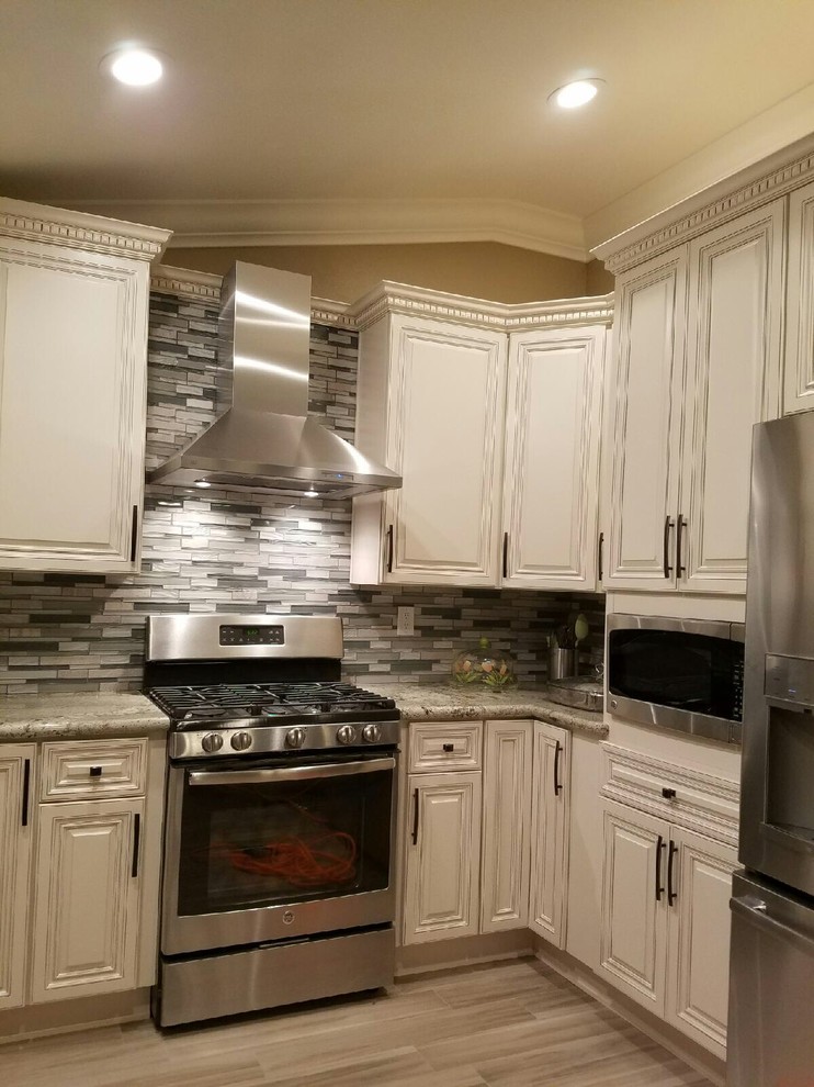 Enclosed kitchen - large traditional l-shaped laminate floor and beige floor enclosed kitchen idea in Orange County with raised-panel cabinets, white cabinets, granite countertops, gray backsplash, matchstick tile backsplash, stainless steel appliances and no island