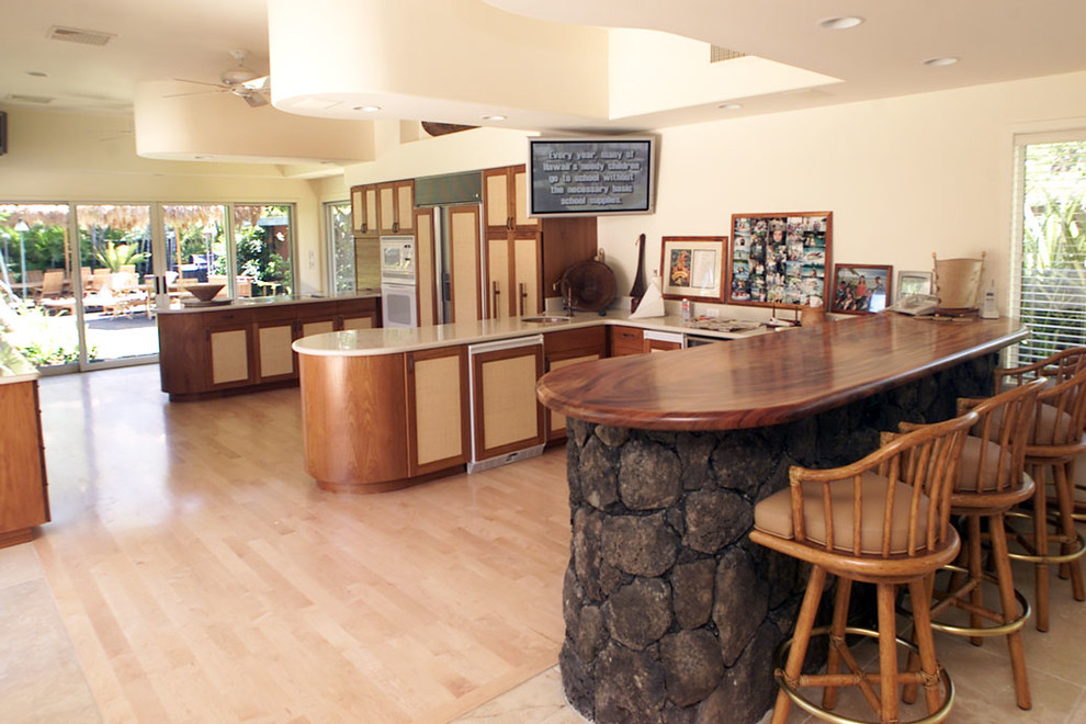 ハワイにある広いトロピカルスタイルのおしゃれなキッチン (シェーカースタイル扉のキャビネット、ベージュのキャビネット、パネルと同色の調理設備、淡色無垢フローリング) の写真