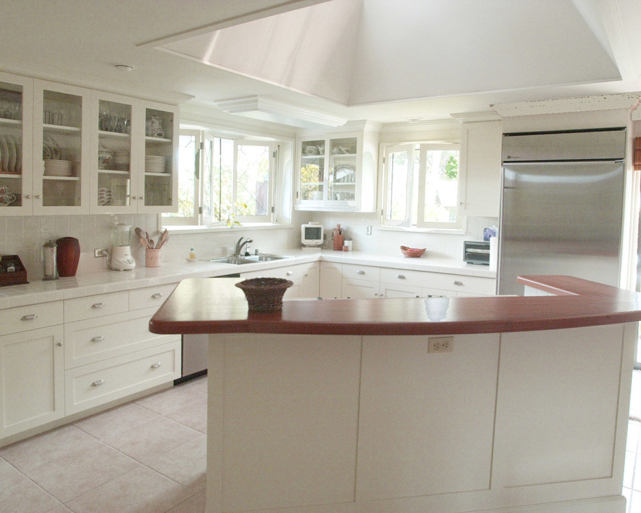 Photo of a large traditional l-shaped kitchen in Hawaii with a built-in sink, glass-front cabinets, white cabinets, tile countertops, white splashback, ceramic splashback, ceramic flooring, an island and stainless steel appliances.