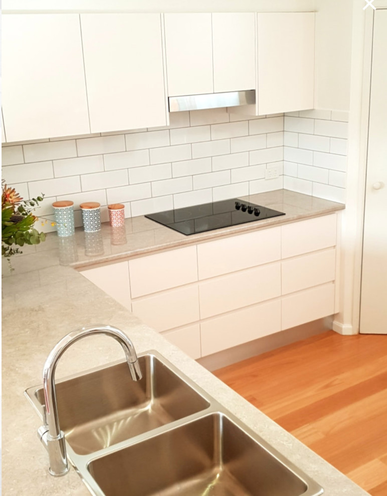 Foto på ett mellanstort funkis kök, med en dubbel diskho, släta luckor, vita skåp, laminatbänkskiva, blått stänkskydd, stänkskydd i tunnelbanekakel, rostfria vitvaror och mellanmörkt trägolv