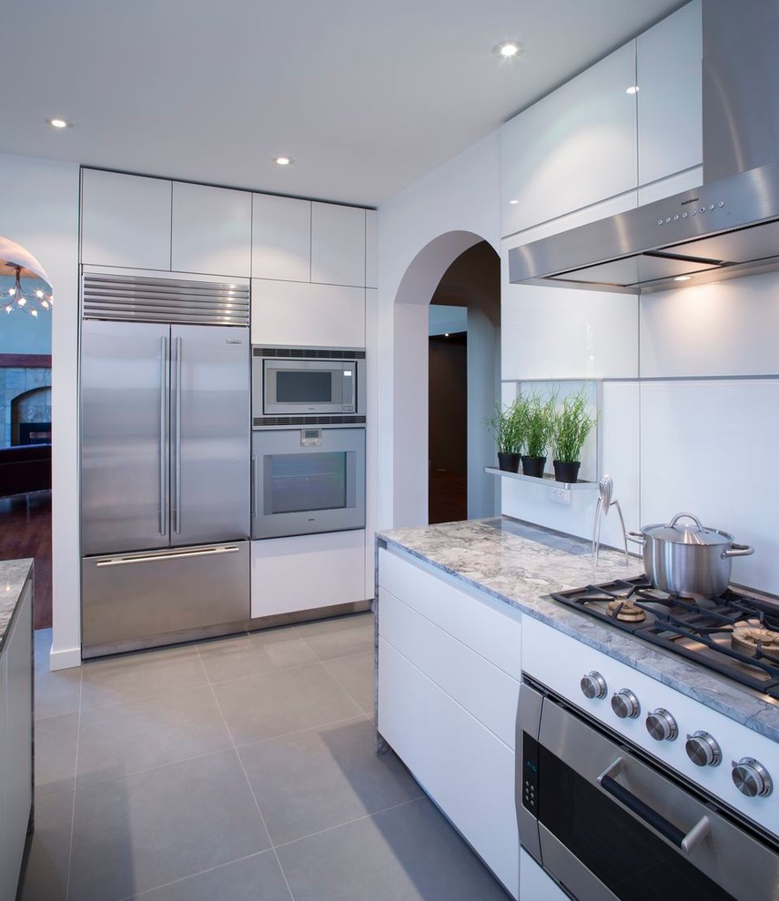 Diseño de cocina contemporánea con armarios con paneles lisos, puertas de armario blancas, salpicadero blanco, electrodomésticos de acero inoxidable y una isla