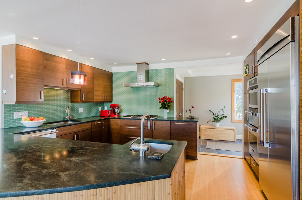 ボストンにある高級な中くらいなコンテンポラリースタイルのおしゃれなキッチン (シングルシンク、フラットパネル扉のキャビネット、中間色木目調キャビネット、ソープストーンカウンター、緑のキッチンパネル、サブウェイタイルのキッチンパネル、シルバーの調理設備、淡色無垢フローリング、ベージュの床) の写真