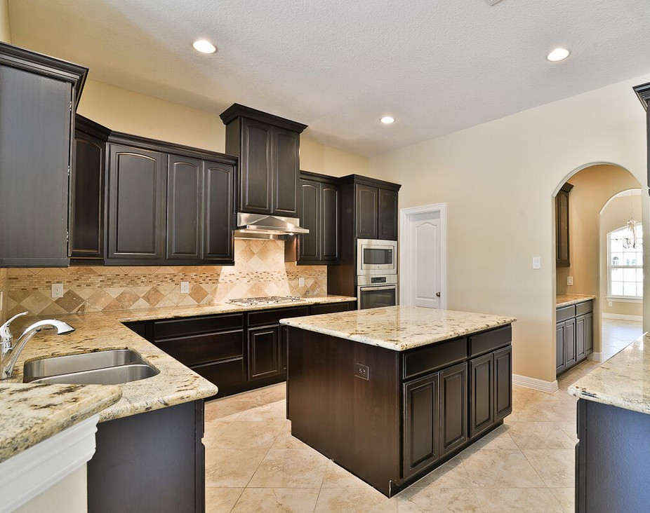 Example of a mid-sized transitional u-shaped travertine floor enclosed kitchen design in Houston with an island, a double-bowl sink, raised-panel cabinets, dark wood cabinets, granite countertops, beige backsplash, ceramic backsplash and stainless steel appliances
