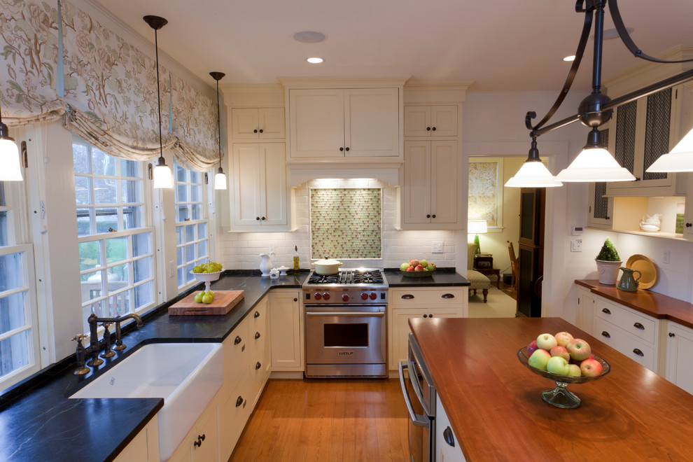 Bild på ett mellanstort lantligt kök, med en rustik diskho, skåp i shakerstil, vita skåp, bänkskiva i täljsten, vitt stänkskydd, stänkskydd i tunnelbanekakel, rostfria vitvaror, mellanmörkt trägolv och en köksö