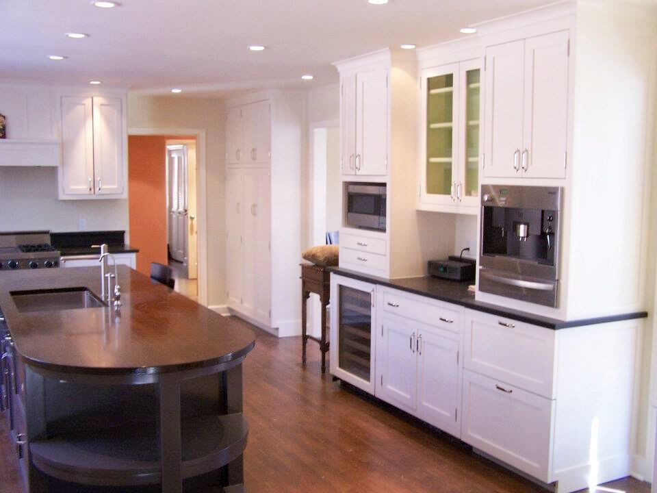 Klassisk inredning av ett kök, med en undermonterad diskho, skåp i shakerstil, vita skåp, träbänkskiva, rostfria vitvaror, mörkt trägolv och en köksö
