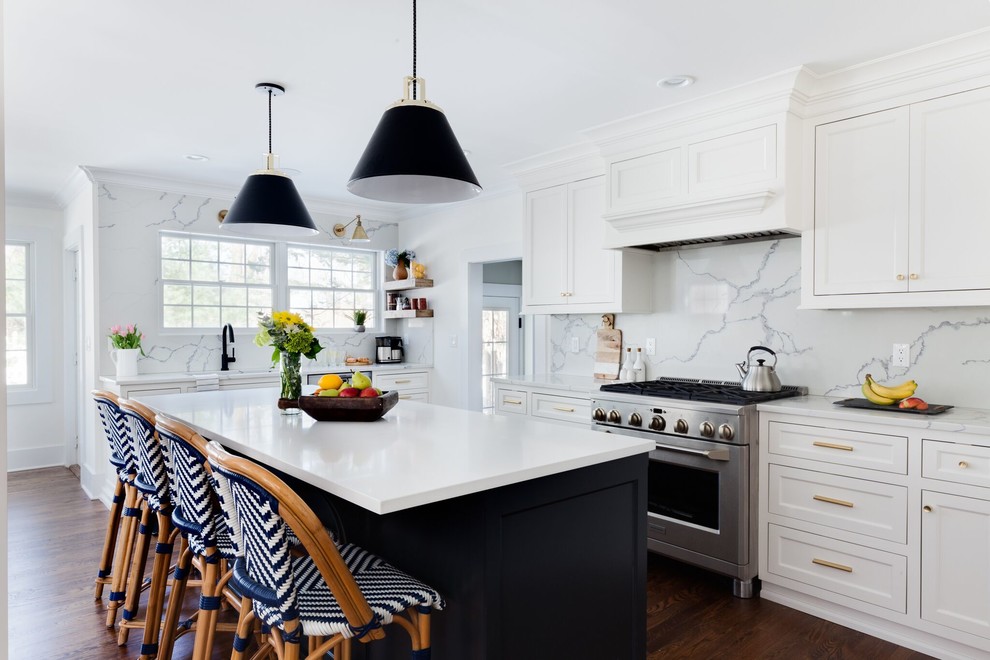 Klassisk inredning av ett kök, med skåp i shakerstil, vita skåp, vitt stänkskydd, stänkskydd i marmor, rostfria vitvaror, mörkt trägolv, en köksö och brunt golv